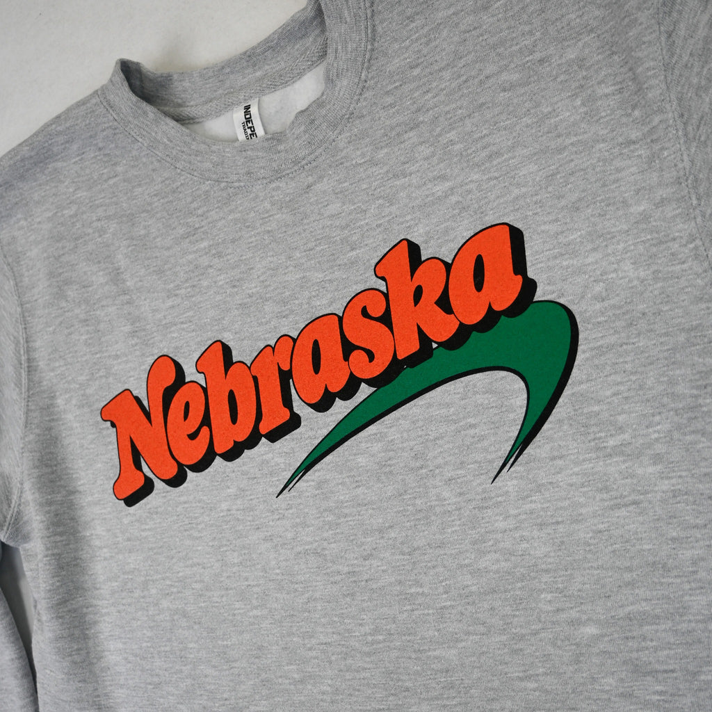 Close-up of orange Nebraska lettering with black shadow and green swoosh on gray crewneck