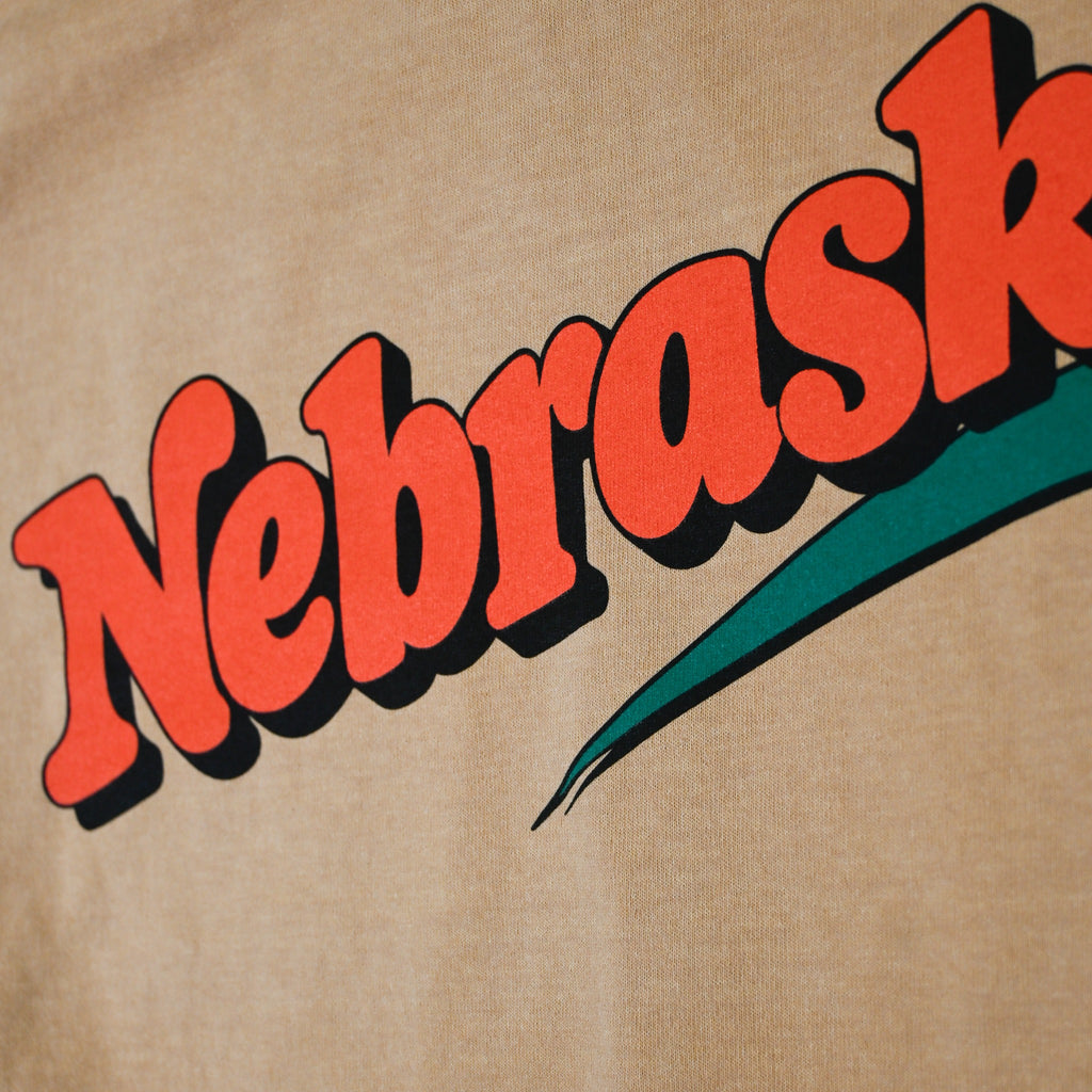 Close-up of orange Nebraska screen-printed lettering and green swoosh on tan T-shirt
