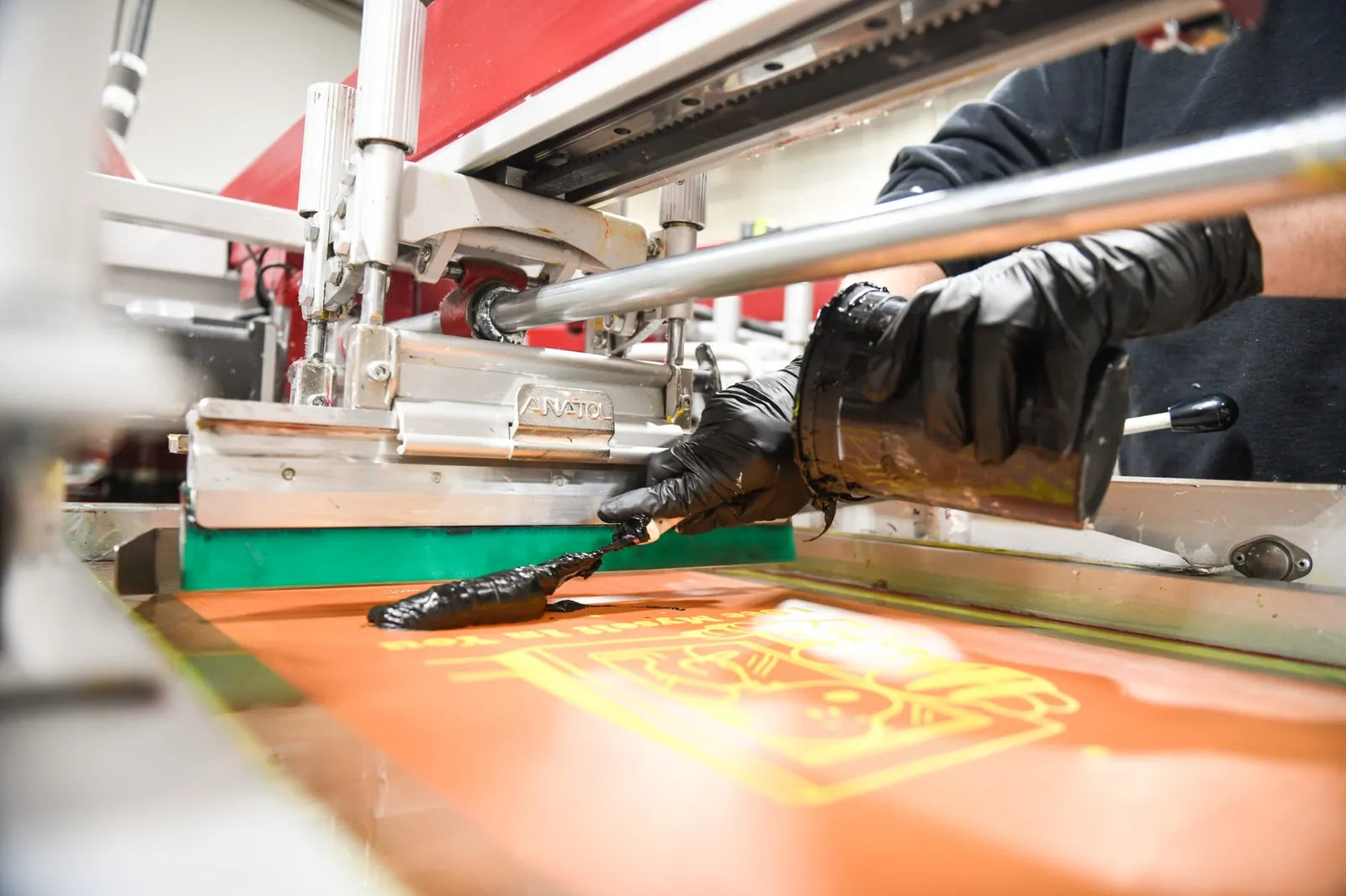Screen printer pulling ink across an artwork screen on the Anatol Volt press